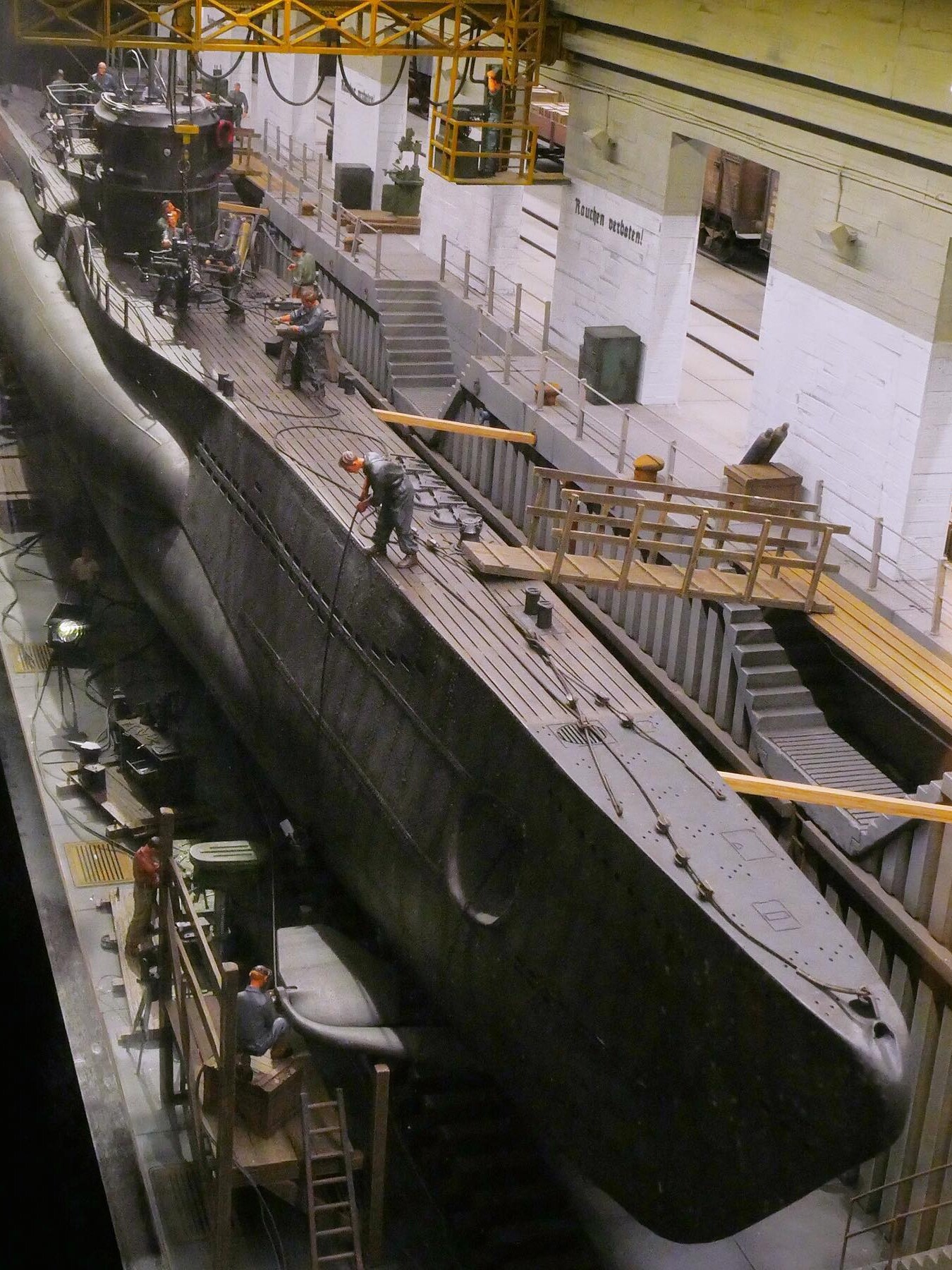 U-Boot im Trockendock mit Arbeitern auf dem Deck und Gerüst, industrielle Halle mit Geländern und Kranbahn im Hintergrund
