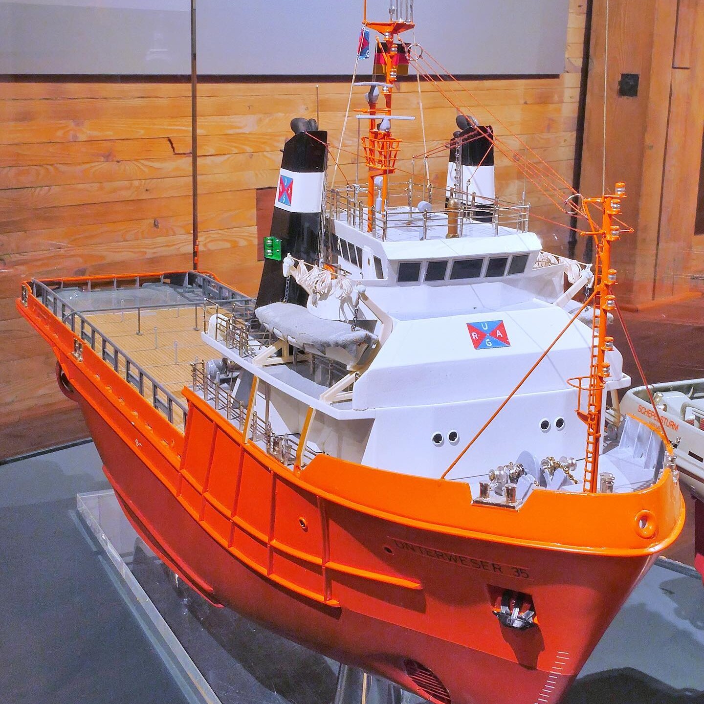 Modell eines orangen Rettungs- oder Forschungsschiffs mit weißer Aufbauten, Brücke, Masten und Decksdetails in einer Ausstellung.