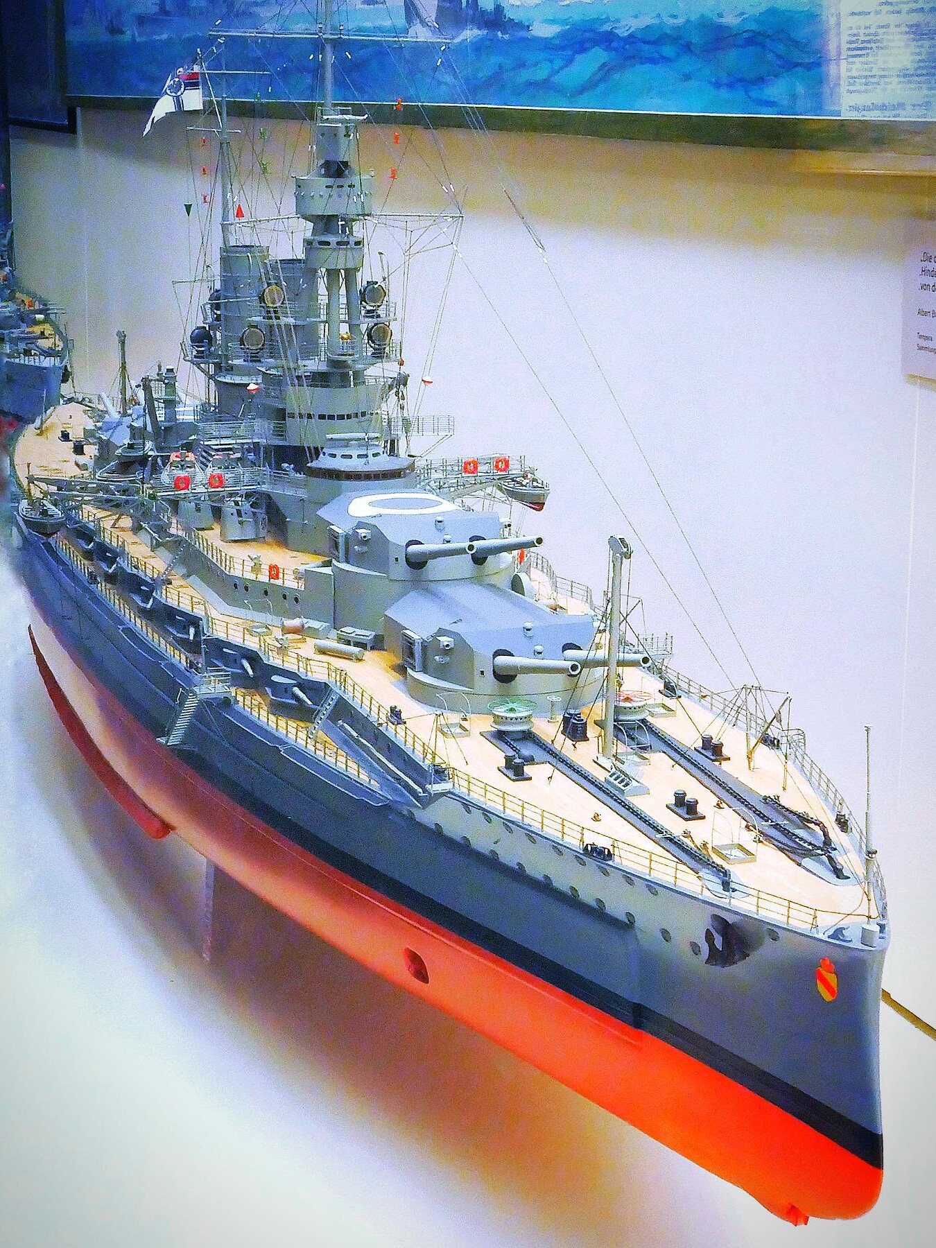 Detailliertes Modell eines grauen Schlachtschiffs mit roten Rumpf, sichtbaren Geschütztürmen, Brückenaufbauten und Takelage in Vitrine