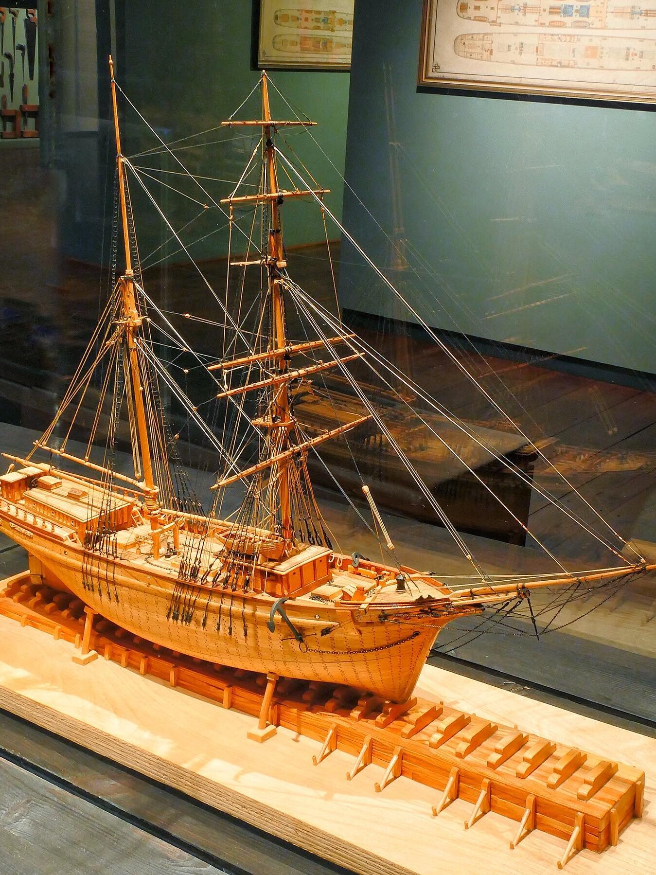 Detailliertes hölzernes Schiffsmodell mit Masten, Takelage und Bugspriet auf Holzgestell in Museumsvitrine.