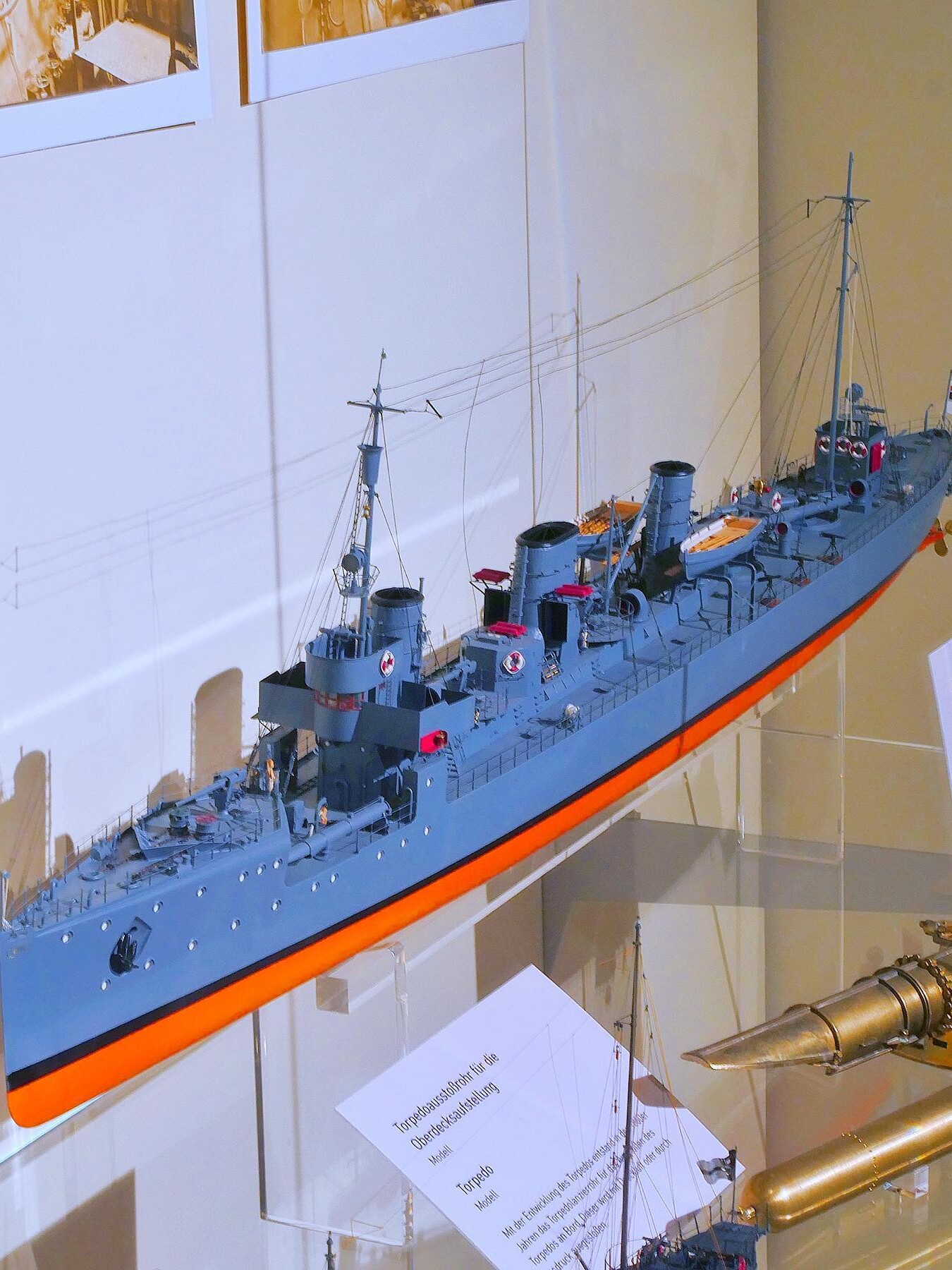Modell eines graublauen Kriegsschiffs mit zwei Schornsteinen, Masten und feinen Takelage-Drähten, auf Ständern in einer Vitrine ausgestellt
